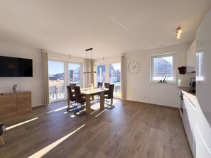 A spacious kitchen with a dining area, large windows, and a flat-screen TV. - The Wangermeer Perle I is a modern, spacious semi-detached house on the Wangermeer - ideal for families and groups looking for comfort and proximity to nature. (Wangerland)