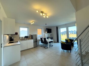 A modern kitchen with a built-in oven, a dining area with a table and chairs, and a living space with a sofa and a TV. - The Wangermeer Perle II is a modern semi-detached house on the Wangermeer and offers a cozy retreat for couples and families. (Wangerland)