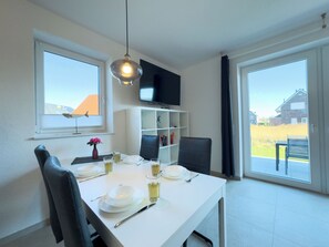 A dining area with a table set for two, a TV mounted on the wall, and a view of the outside. - The Wangermeer Perle II is a modern semi-detached house on the Wangermeer and offers a cozy retreat for couples and families. (Wangerland)