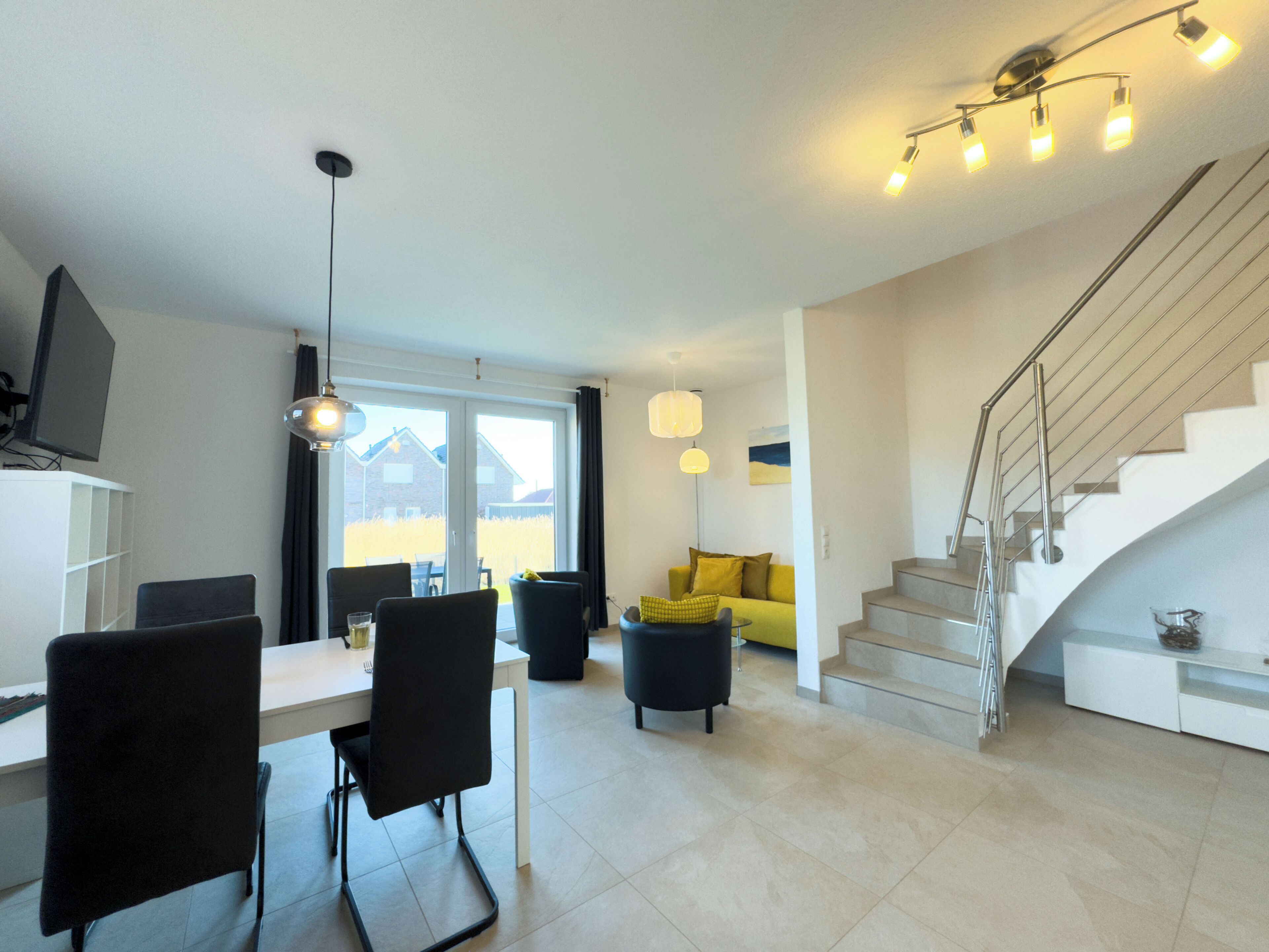 Ein stilvolles Wohnzimmer mit Essbereich, einer Couch, einer Treppe und Blick ins Freie.