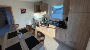 A modern kitchen with wooden cabinets, a dining area with a table and chairs, and a window providing natural light. - The Wangernest vacation home offers family-friendly comfort in the immediate vicinity of the Wangermeer and its own private beach. (Wangerland)