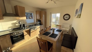 A compact kitchen with wooden cabinets, a built-in oven, and a dining area with a table and chairs. - The Wangernest vacation home offers family-friendly comfort in the immediate vicinity of the Wangermeer and its own private beach. (Wangerland)