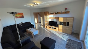 A living room with a sofa, coffee table, TV, and wooden cabinets. - The Wangernest vacation home offers family-friendly comfort in the immediate vicinity of the Wangermeer and its own private beach. (Wangerland)