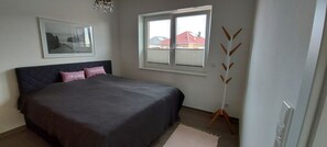 A bedroom with a bed, a window, a coat rack, and a framed picture on the wall.