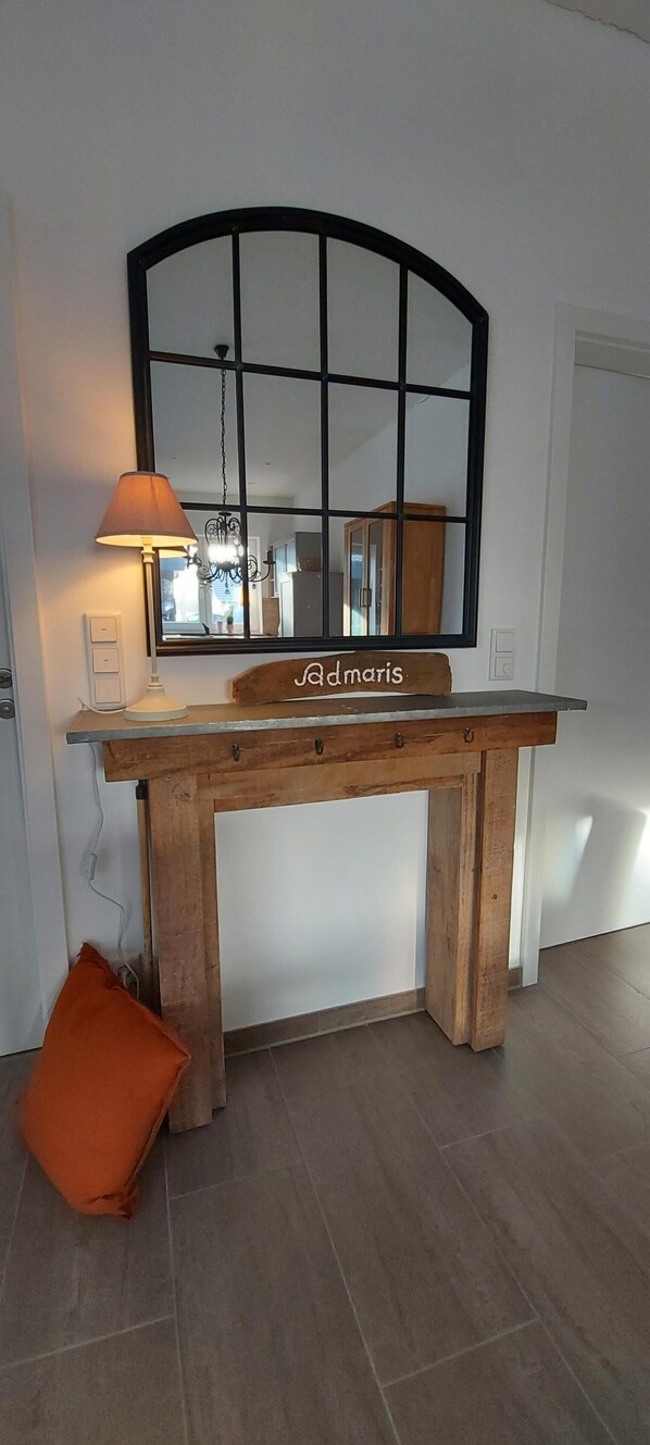 A wooden table with a mirror above it, a lamp on the left, and an orange cushion on the floor.