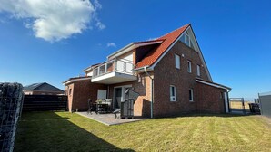 Punatiilinen, kaksikerroksinen talo, jossa on punainen katto, parveke ja ulkokalusteilla varustettu terassi.