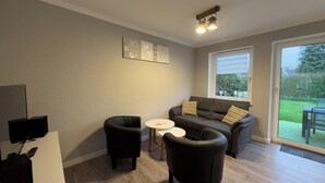 A living room with a sofa, two armchairs, a small table, a TV, and a window with a view of the outdoors. - The Windfang 2 vacation home in Hooksiel offers modern comfort, a quiet location and a sunny terrace - perfect for relaxing days by the North Sea. (Hooksiel)