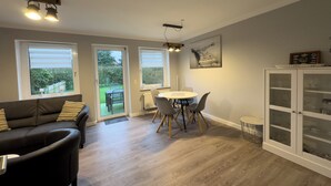 A modern living room with a sofa, dining table, chairs, and a cabinet. - The Windfang 2 vacation home in Hooksiel offers modern comfort, a quiet location and a sunny terrace - perfect for relaxing days by the North Sea. (Hooksiel)