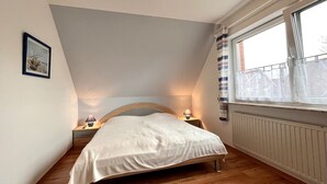 Een slaapkamer met een bed, nachtlampjes, een raam met gordijnen en een radiator.