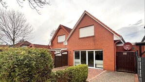 Een tweelaags bakstenen huis met een verharde oprit, een hekpoort en een grote schuifdeur van glas.