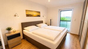 Un dormitorio moderno con una cama doble, mesitas de noche, una lámpara de noche, una planta en maceta y un cuadro en la pared.