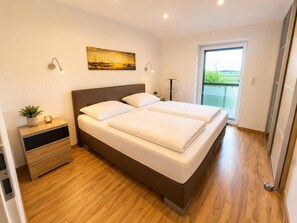 A modern bedroom with a double bed, bedside tables, a nightstand, a potted plant, and a painting on the wall. - Comfortable vacation home "Austernfischer" in Wangerland near the North Sea with sauna, 3 bedrooms for up to 5 guests - dogs welcome. (Wangerland)