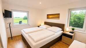 Un dormitorio moderno con una cama grande, mesitas de noche, un televisor y vistas a zonas verdes.