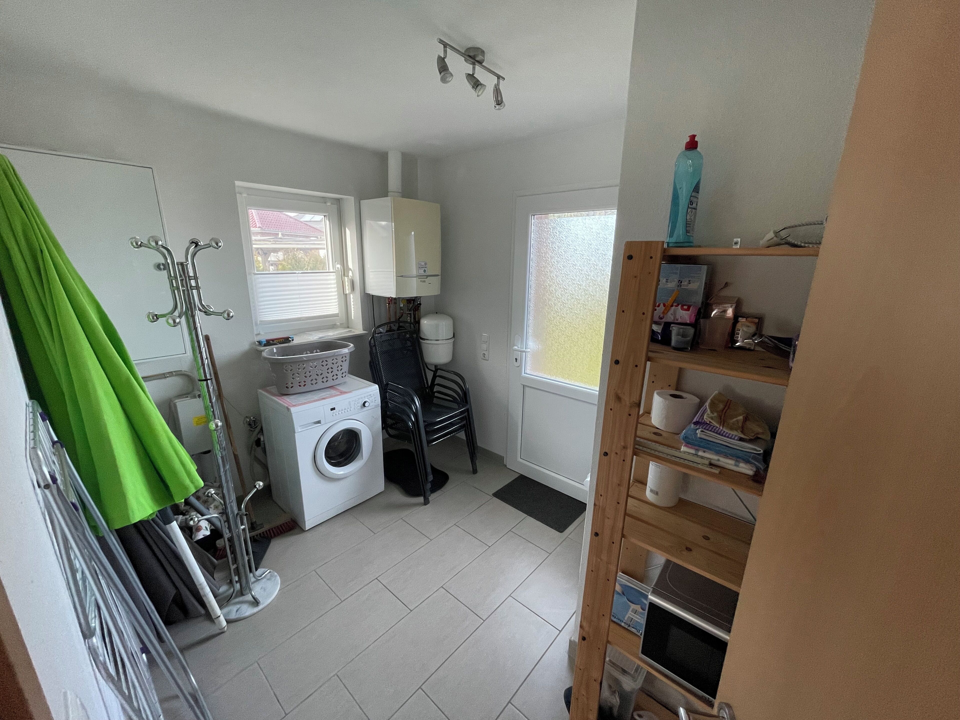 A laundry room with a washing machine, drying rack, and shelves with cleaning supplies.