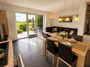 A modern dining area with a large table, chairs, and a view through glass doors to an outdoor patio. - Cozy vacation home "Sturmmöwe" in Wangerland near the North Sea with sauna, 2 bedrooms for up to 3 guests - dogs welcome. (Wangerland)