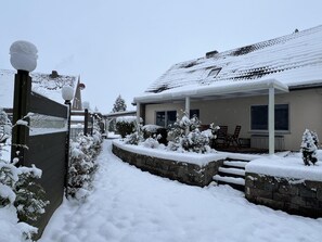 A snow-covered residential area with a house, a covered patio, and a stone wall.