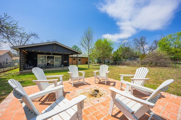 Een terras met vier Adirondack-stoelen, een vuurkorf en een modern huis op de achtergrond.
