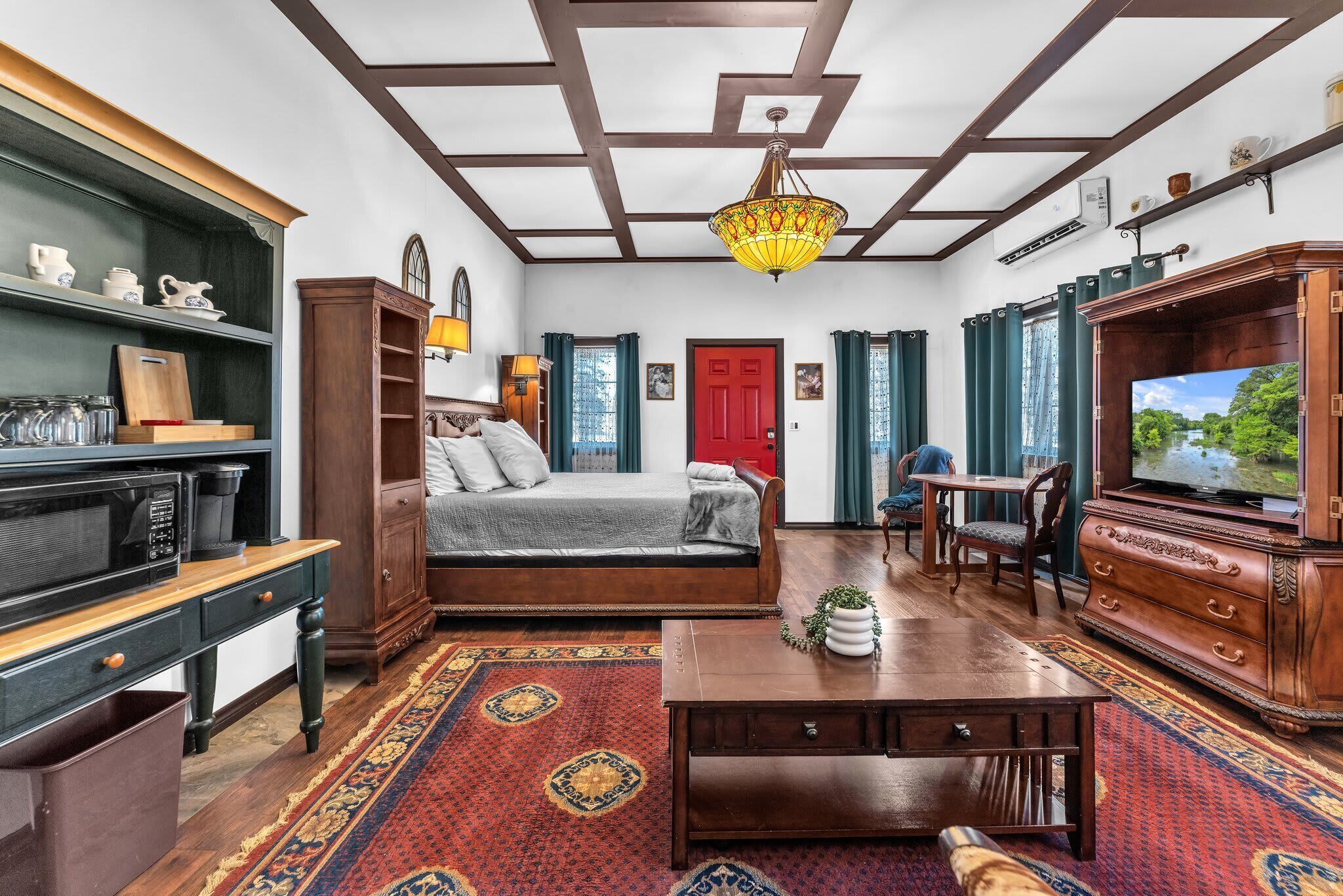 A room with a bed, a desk, a television, and a red door.