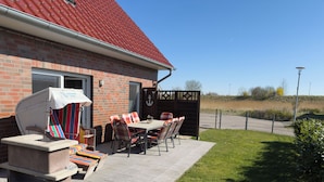 Un patio con tavolo e sedie, un barbecue e una casa in mattoni con tetto rosso.