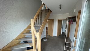 Una scala con ringhiere in legno che conduce a un pianerottolo, un corridoio con pavimento piastrellato e una porta con pannello di vetro.
