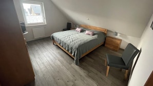 Ein Schlafzimmer mit Bett, Stuhl, Schreibtisch, Fenster und Heizkörper.