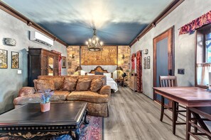 A room with a sofa, a dining table, a chandelier, and a stone wall. - The Vineyards: Cabin 2 - Private Hot Tub & Shared Pool (Fredericksburg)