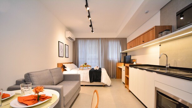 Quarto de hotel moderno com cozinha compacta, área de refeições e cama com cortinas.