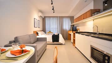 Una habitación de hotel moderna con kitchenette, zona de comedor y cama con cortinas.