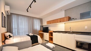 Quarto de hotel moderno com duas camas, uma cozinha compacta e uma janela grande com cortinas.