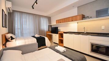Una habitación de hotel moderna con dos camas, una kitchenette y un amplio ventanal con cortinas.