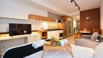 A modern hotel room with a bed, a TV, a kitchenette, and a dining area.