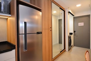 A modern kitchen with a stainless steel refrigerator, wooden cabinets, and a built-in microwave. - Studio em frente a UFSC e HU - 319A (Florianópolis)