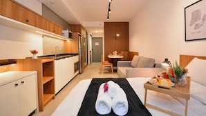 A modern hotel room with a kitchenette, a dining area, and a bed with towels and breakfast items. - Studio em frente a UFSC e HU - 319A (Florianópolis)