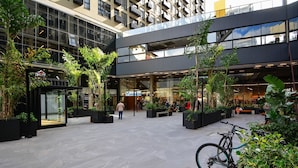 An urban plaza with modern buildings, outdoor seating, and greenery. - Studio em frente a UFSC e HU - 319A (Florianópolis)