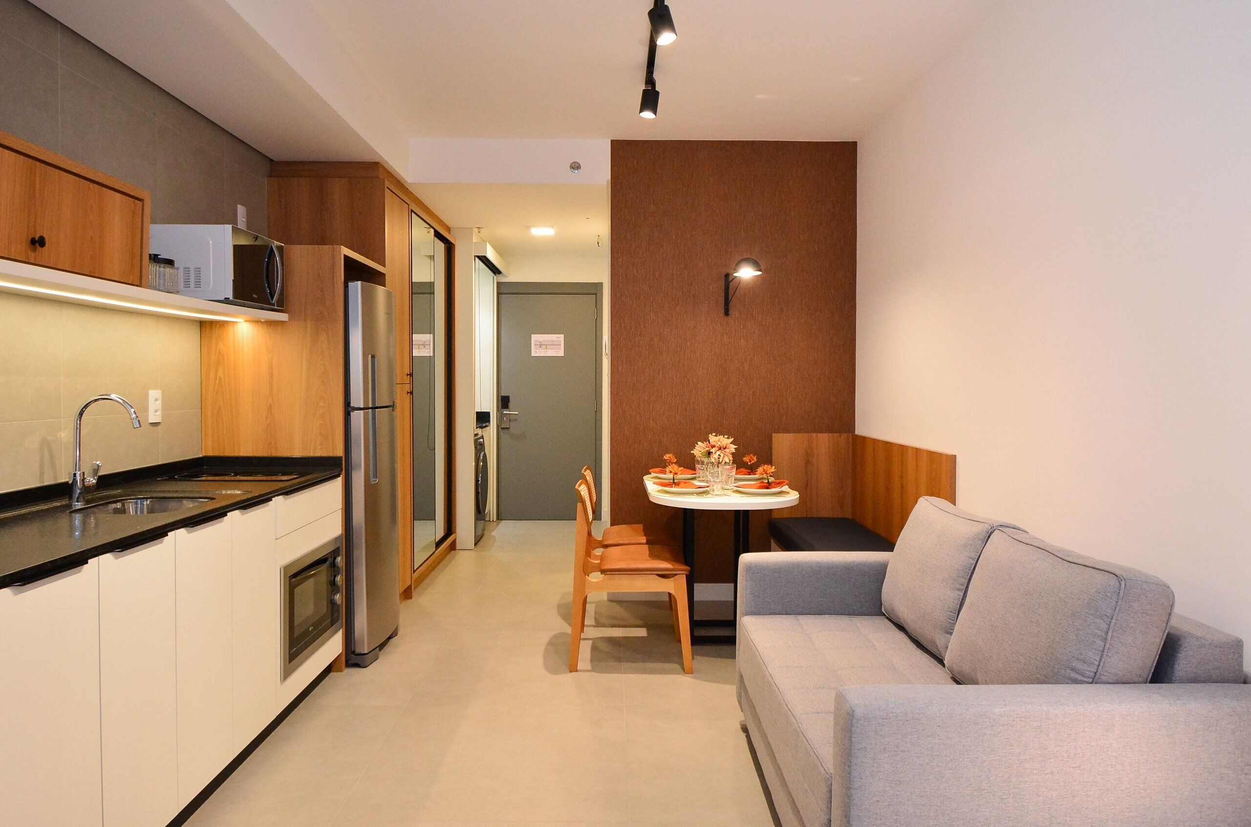 Une cuisine compacte dotée d’appareils électroménagers modernes, un coin repas avec une table et des chaises, et un canapé gris.