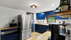 Une cuisine moderne dotée d’appareils électroménagers en acier inoxydable, de meubles bleus, d’un plan de travail en bois et d’une machine à café noire.