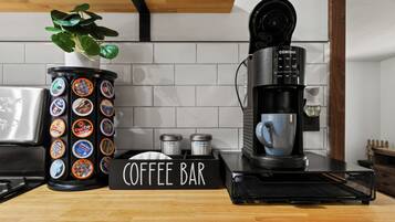 Een koffiebar inrichting met een koffieapparaat, een container koffiekapsules, suiker en melk, en een bordje met de tekst 'COFFEE BAR'.