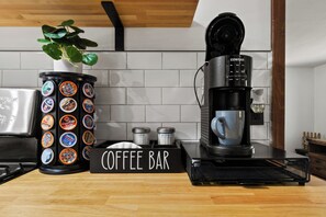 A coffee bar setup with a coffee machine, a container of coffee pods, sugar and creamer containers, and a sign labeled 'COFFEE BAR'. - Charming Cottage by Lake Ontario | Firepit + Yard (Richland)