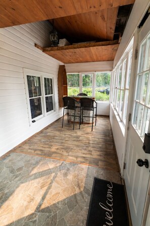 A covered porch with a stone floor, a wooden ceiling, and a table with chairs.