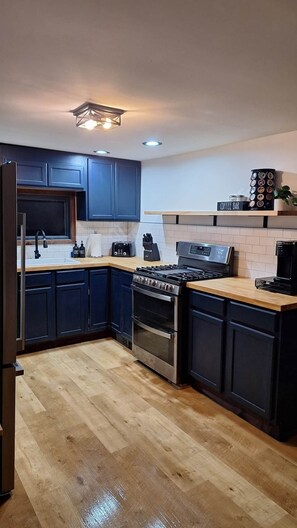 A modern kitchen with dark blue cabinets, a stainless steel stove, a coffee maker, and a sign labeled 'Coffee Bar'.