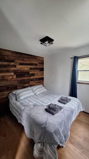 A bedroom with a wooden headboard, a bed with striped bedding, a knitted throw, and a window with curtains.