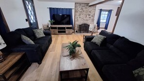A living room with two black sofas, a wooden coffee table, a television, and a stone wall.