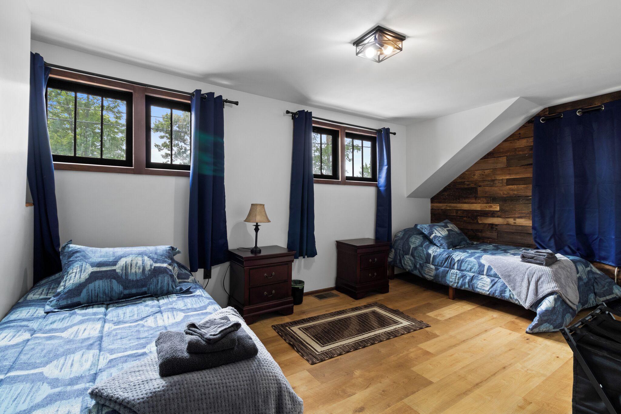 A bedroom with two beds, a dresser, a lamp, and a window with curtains.