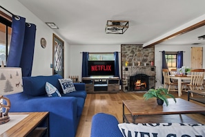 Un saló amb un sofà blau, una taula de centre, una llar de foc i un televisor que mostra 'NETFLIX'.