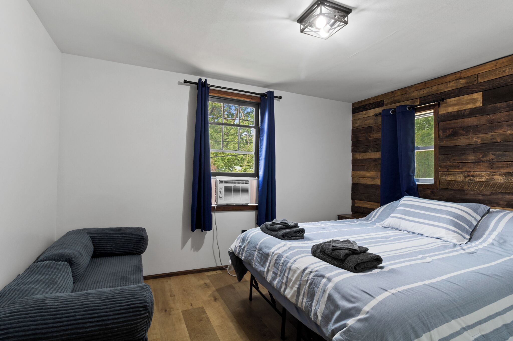 Une chambre à coucher avec un lit, une chaise, une fenêtre avec des rideaux et un mur en bois.