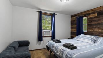Een slaapkamer met een bed, een stoel, een raam met gordijnen en een houten wand.