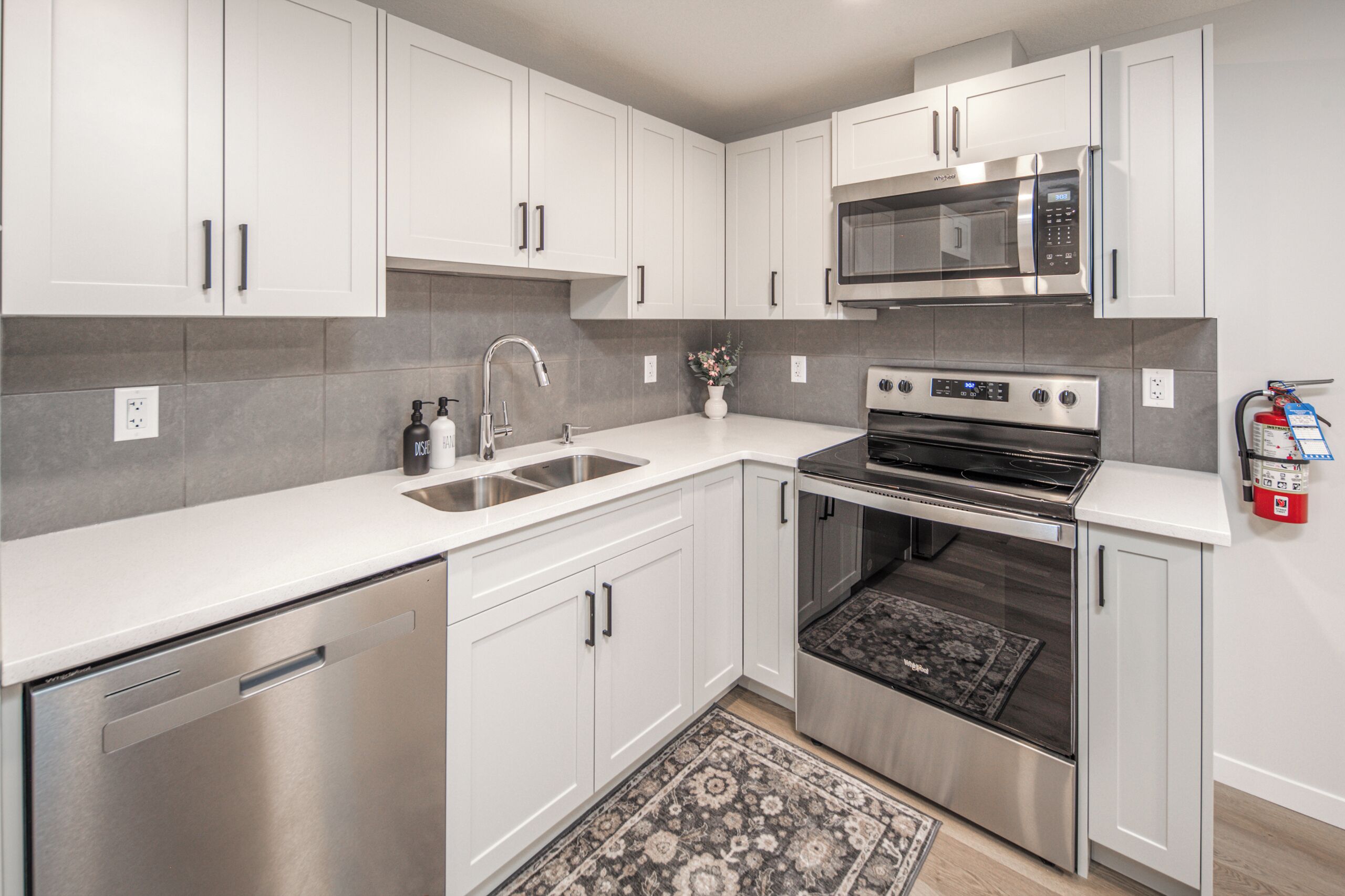 A modern kitchen with white cabinets, stainless steel appliances, a microwave, oven, and a dishwasher.