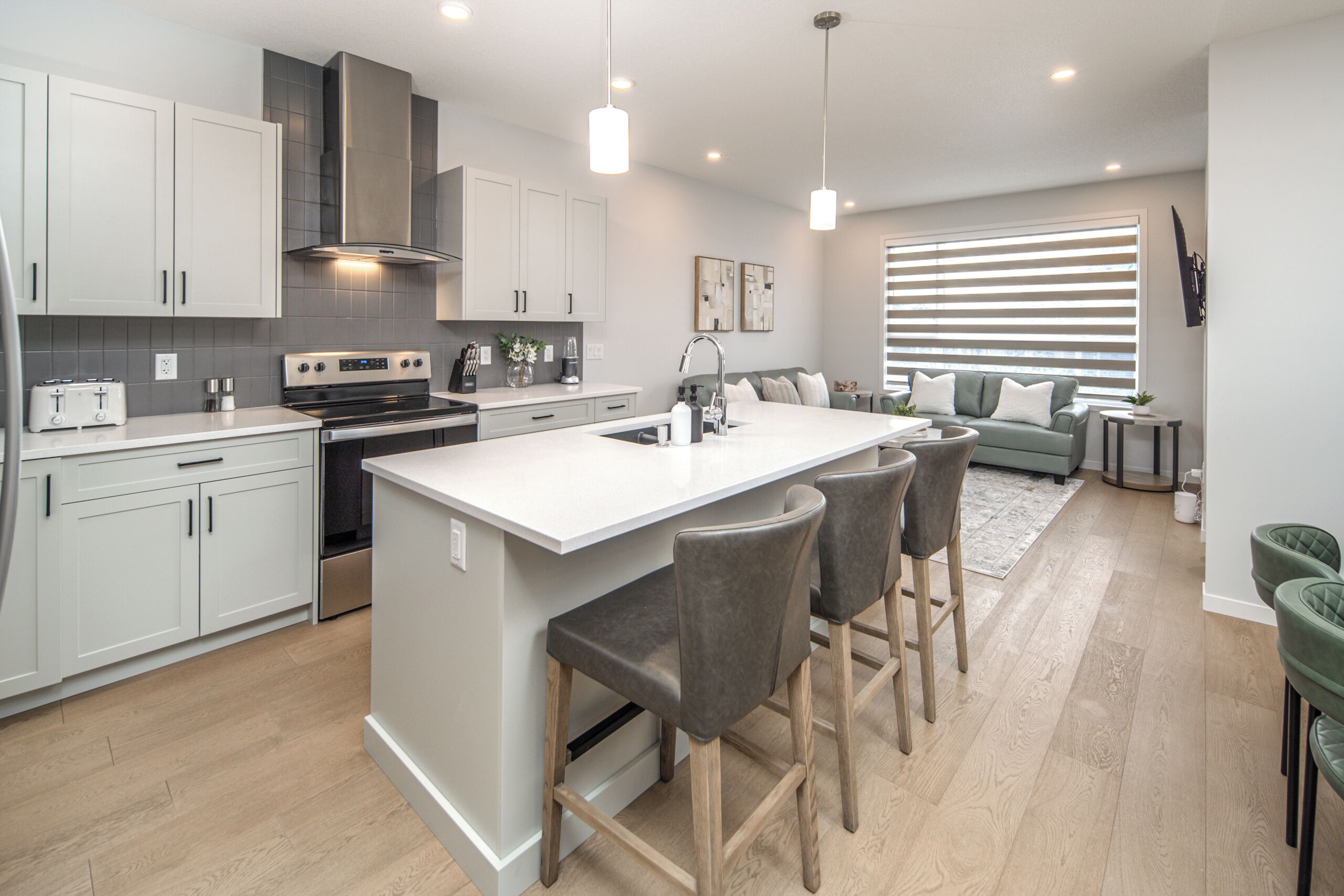 A modern kitchen with a central island, bar stools, and a dining area with a sofa and side table.