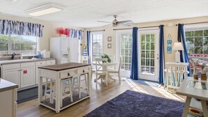 Une cuisine bien éclairée, avec des meubles blancs, une table en bois et un coin repas équipé de chaises.
