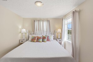 A bedroom with a large bed, two bedside tables with lamps, a window with curtains, and a ceiling light. - Island Palms- Pet Freindly- 3 Bedroom SGI (Saint George Island)